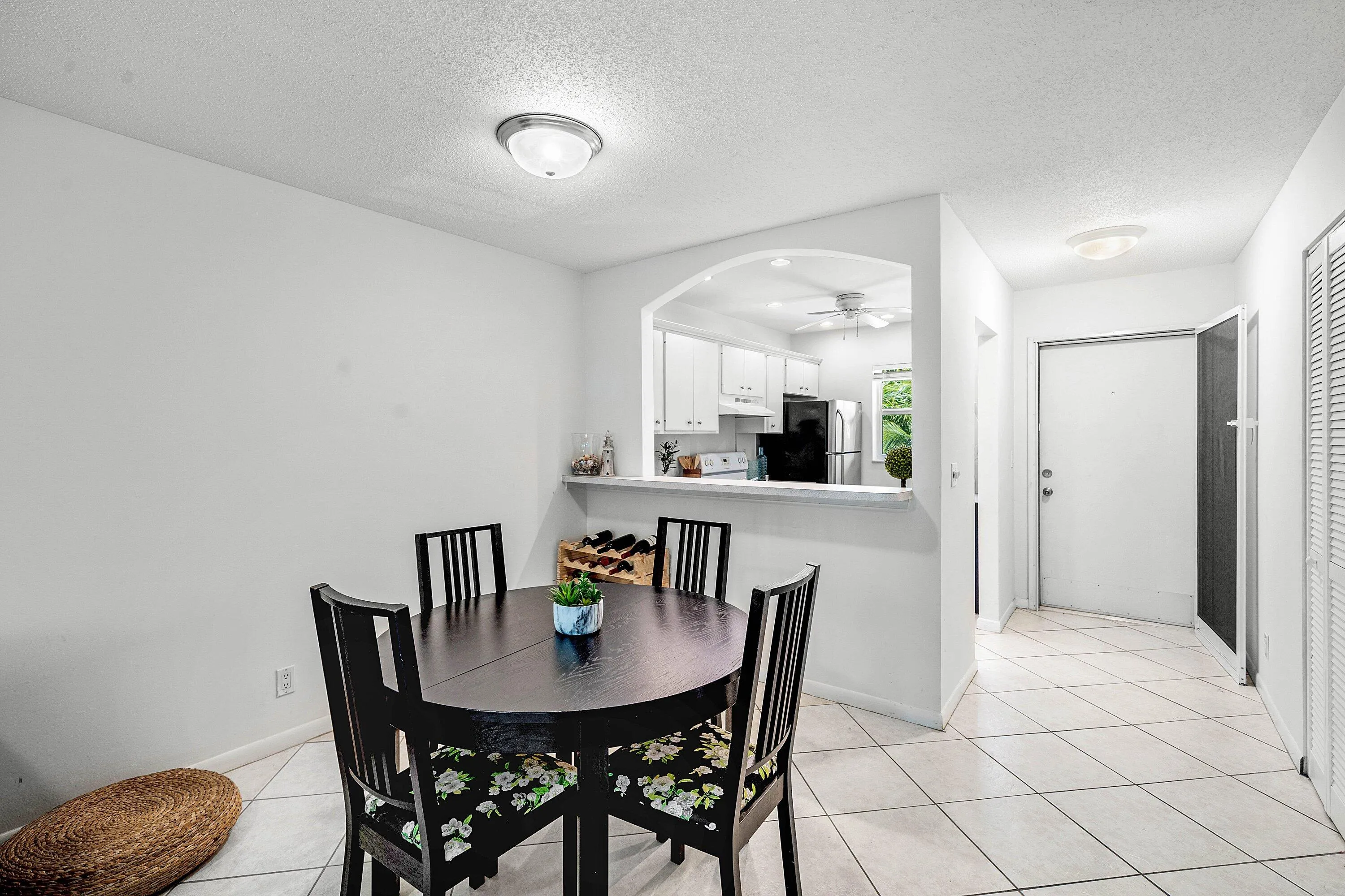 Bright dining area featuring a round table with seating for four, ceramic tile flooring, and a pass-through window to the kitchen