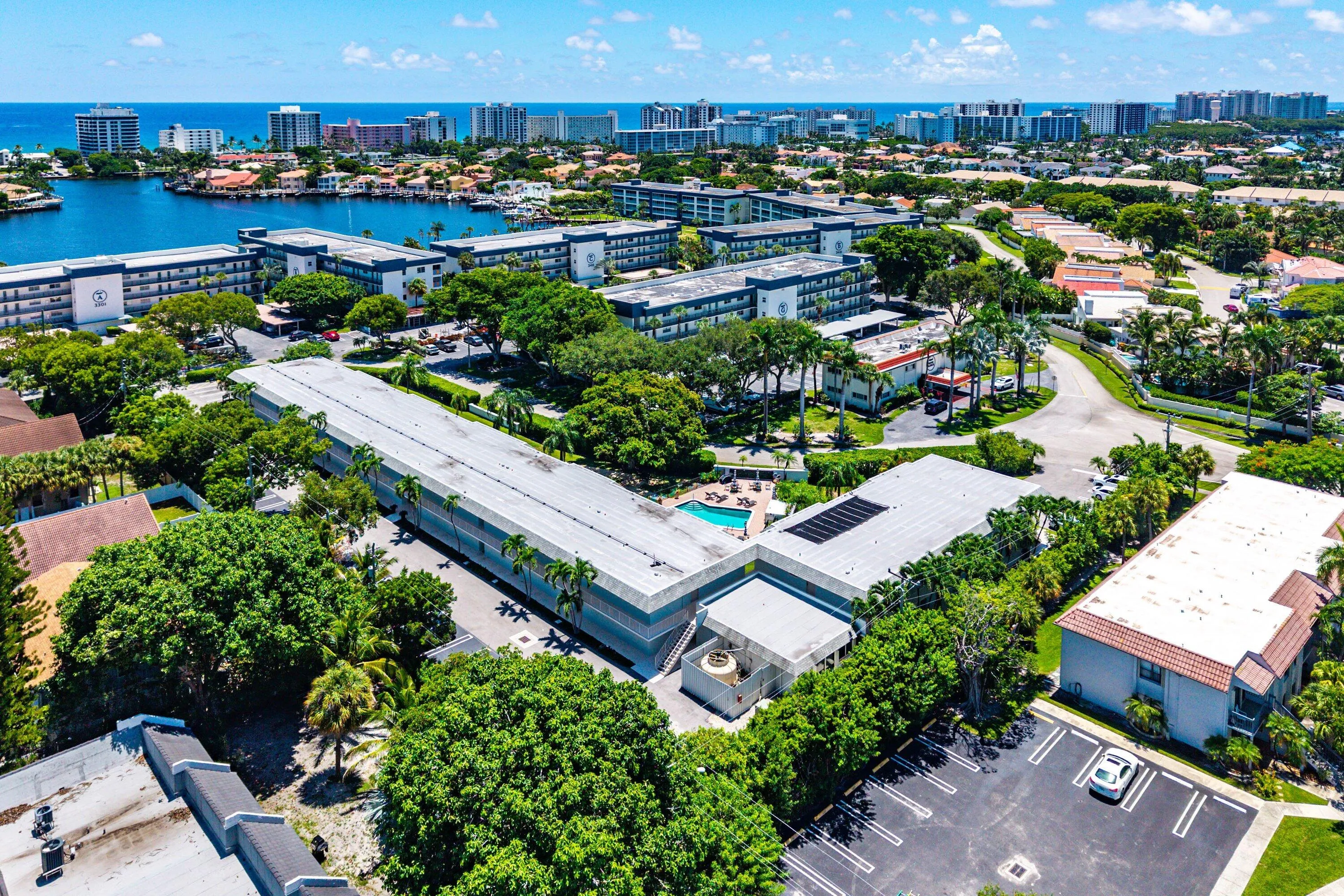 Aerial property overview featuring multiple buildings, lush tropical landscaping, and an outdoor swimming pool