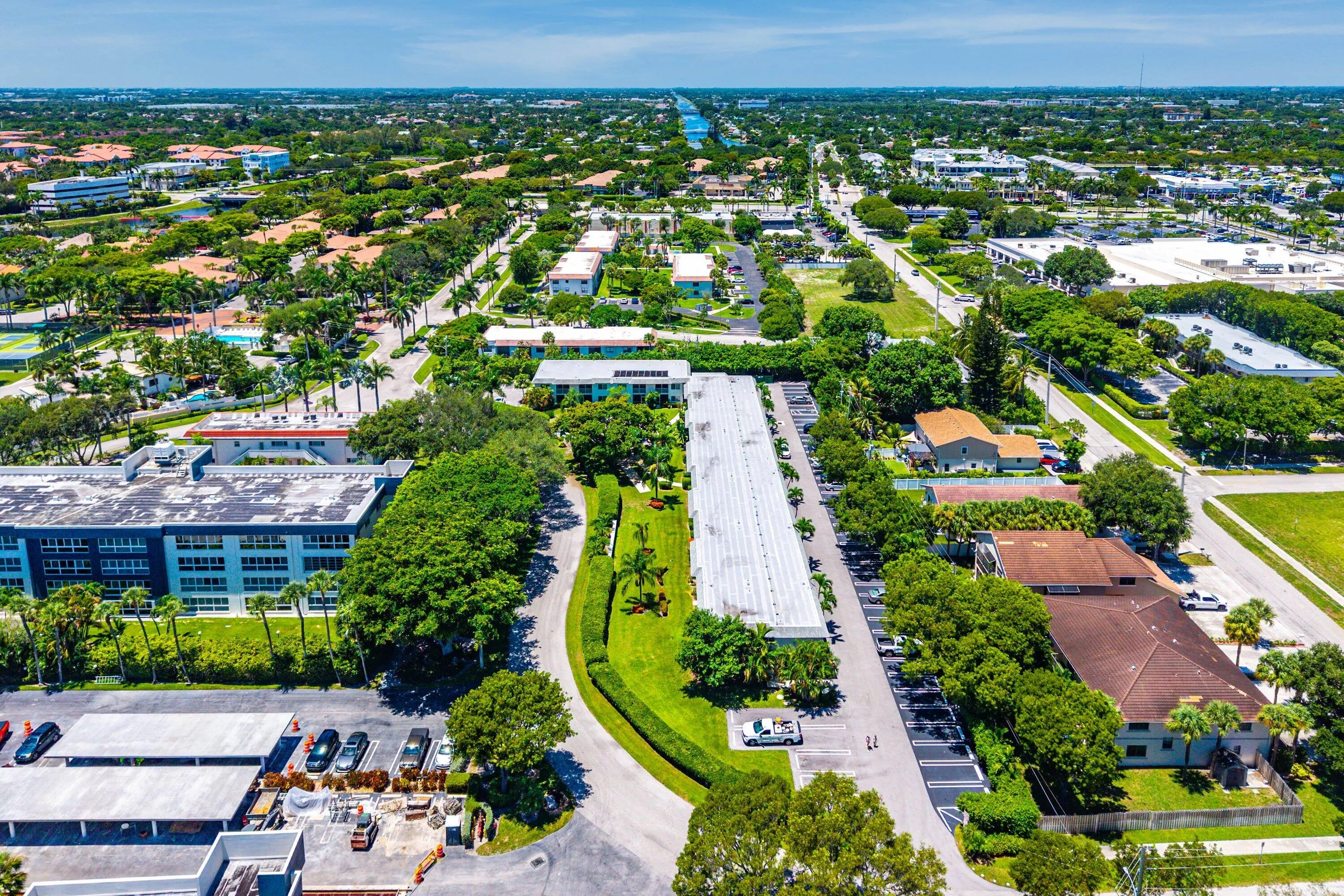 Expansive aerial perspective showcasing a vibrant community with abundant green spaces, a canal feature, and multiple residential and commercial structures