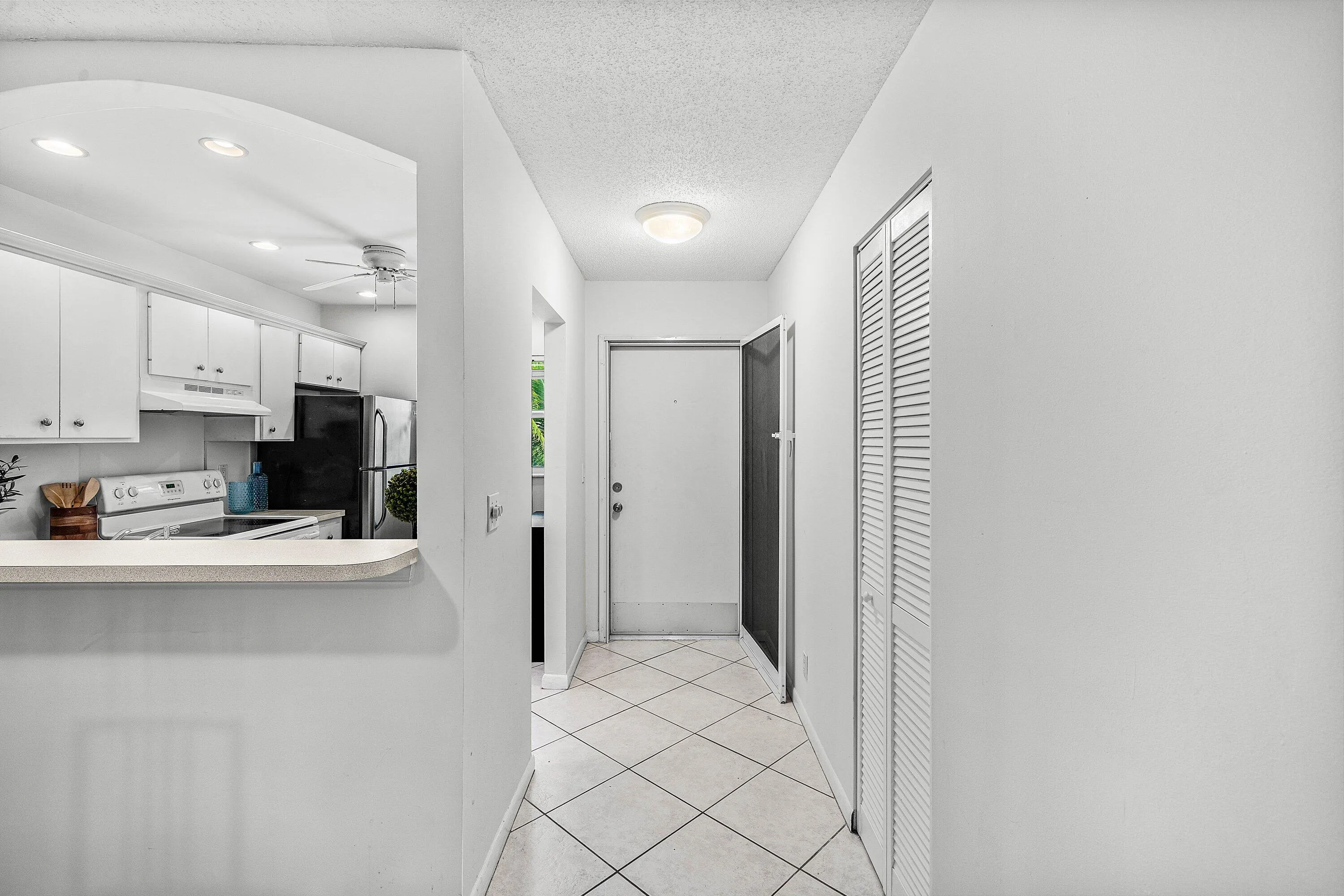 White kitchen cabinetry with black appliances, archway opening, tiled flooring, and louvered closet doors