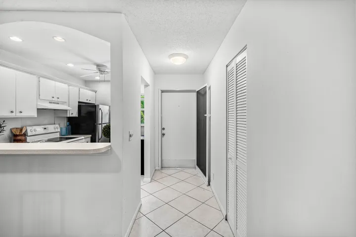 White kitchen cabinetry with black appliances, archway opening, tiled flooring, and louvered closet doors