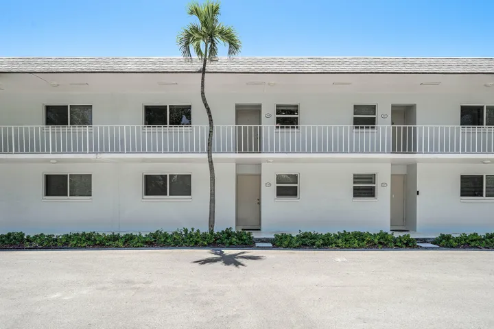 Two-story facade with white exterior, white balcony railings, and ground-level landscaping