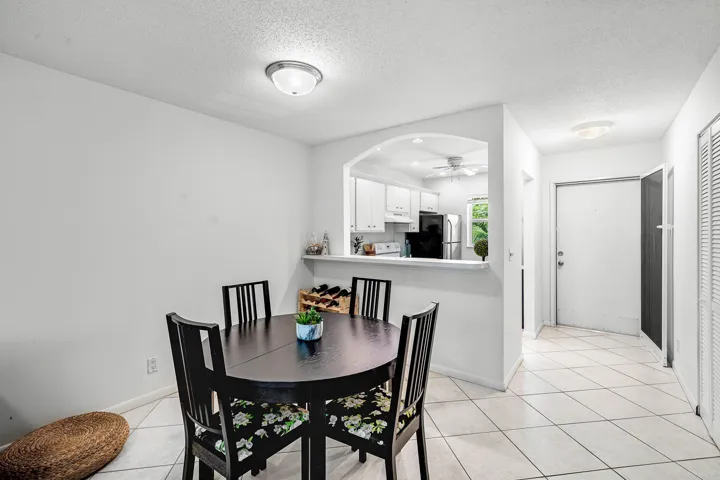 Bright dining area featuring a round table with seating for four, ceramic tile flooring, and a pass-through window to the kitchen