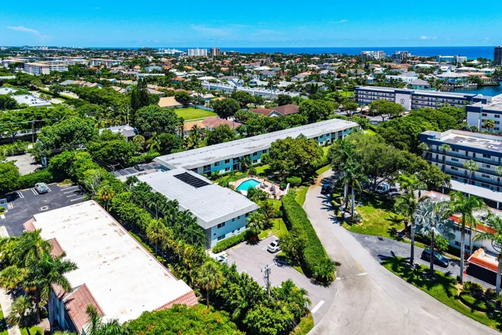 Aerial perspective showcasing multiple buildings, lush landscaping, a swimming pool, and proximity to a body of water and distant cityscape