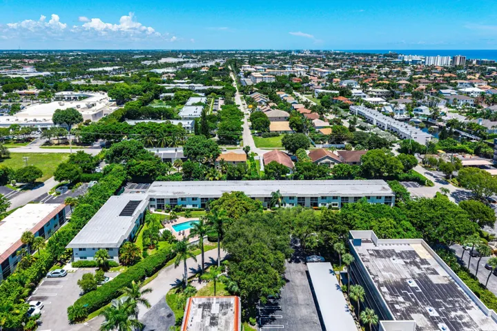 Aerial perspective of residential buildings with an outdoor swimming pool, surrounded by mature trees and paved parking areas