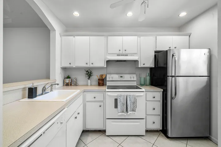 White cabinetry, light-toned countertops, white tile flooring, and a stainless steel refrigerator