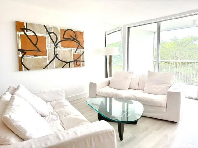 Living area with light wood-finish flooring, a full wall of sliding glass doors, and a balcony with metal railings