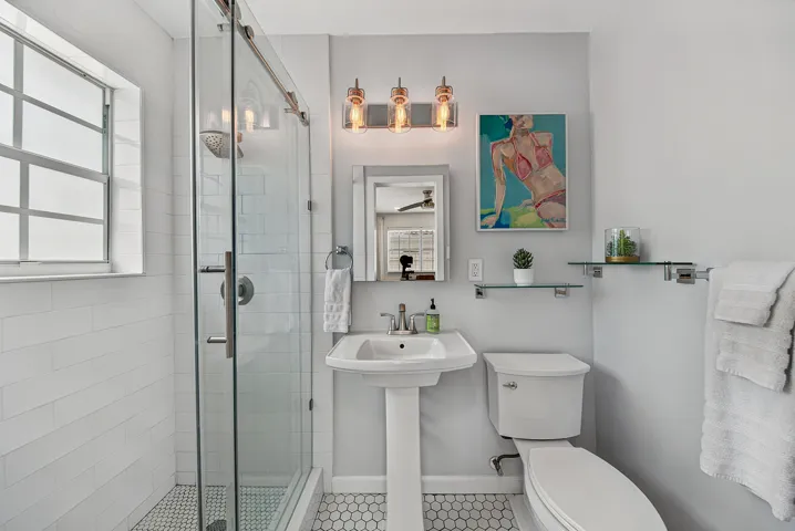 Spa-inspired bathroom featuring a walk-in shower with glass enclosure and tile surround, pedestal sink, toilet, and mosaic tile flooring