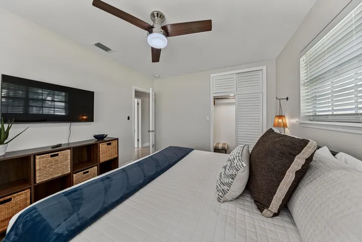 Ceiling fan with integrated lighting, wall-mounted light fixture, louvered closet doors, window with blinds, and light-toned wall paint
