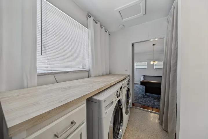 Light wood-finish countertop over laundry appliances, white cabinetry with silver hardware, and a window with blinds