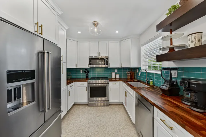 Kitchen featuring white cabinetry, warm wood-finish countertops, a teal subway tile backsplash, stainless steel appliances, and a built-in sink