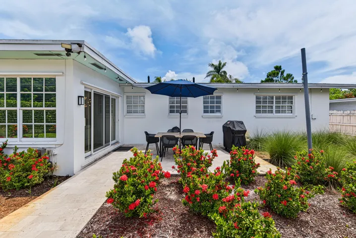 Exterior patio with a paved surface, impact sliding glass doors, white exterior walls, and landscaped garden beds