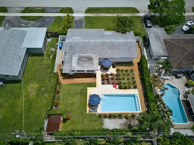 Aerial view of this residence showcasing a resort-style backyard featuring a heated swimming pool with surrounding concrete decking, mature landscaping with established trees, manicured lawn areas, and patio