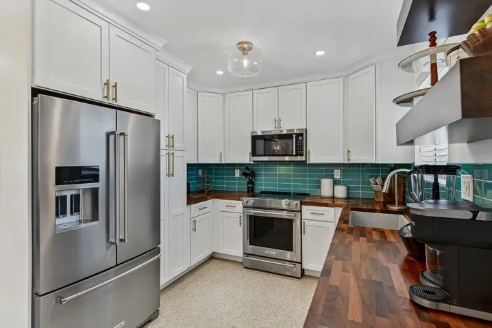 Modern kitchen featuring white shaker cabinetry with brushed nickel hardware, stainless steel French-door refrigerator and convection range, teal subway tile backsplash, wood-finish island countertop with seating, and recessed ceiling lighting throughout