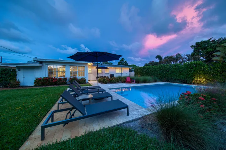 Backyard featuring a rectangular swimming pool, a surrounding patio, lush green lawn, and mature perimeter hedging