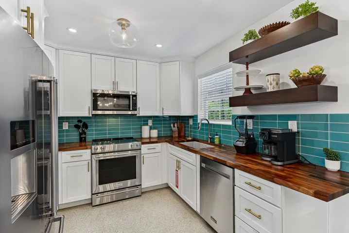 White cabinetry with gold-tone hardware, wood-finish countertops, stainless steel appliances, teal subway tile backsplash, and recessed lighting