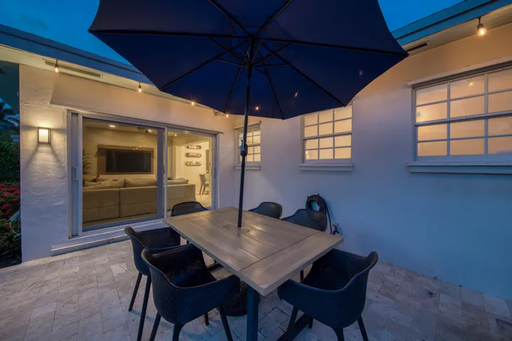 Sophisticated outdoor entertaining space featuring a paver patio with dining table seating for four, navy market umbrella for shade, and ambient wall-mounted lighting