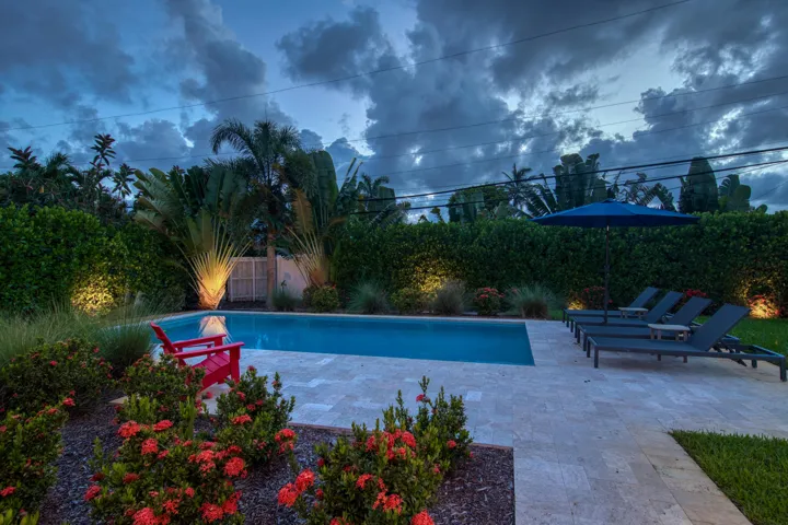 Swimming pool with a light-toned paved deck, surrounded by mature landscaping, and integrated landscape lighting
