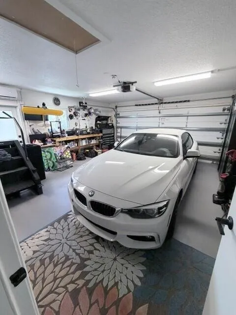 Attached two-car garage featuring a sectional garage door, overhead fluorescent lighting, a window-mounted air conditioning unit, and attic access