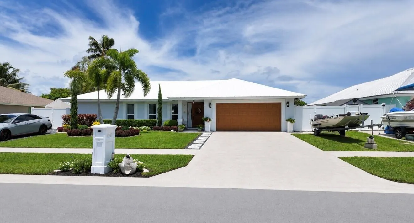 Lush green lawn with tropical landscaping, a white metal roof, and a wood-finish garage door