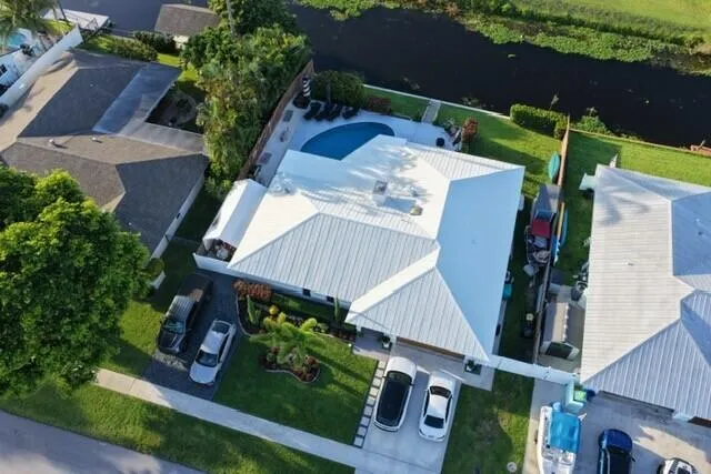 This impressive aerial view showcases the home's beautifully landscaped curb appeal, spacious lot, and inviting entrance. From above the properties prime canal-front setting, and private pool.
