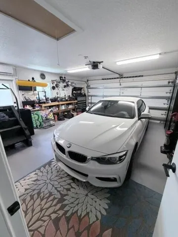 Attached two-car garage featuring a sectional garage door, overhead fluorescent lighting, a window-mounted air conditioning unit, and attic access