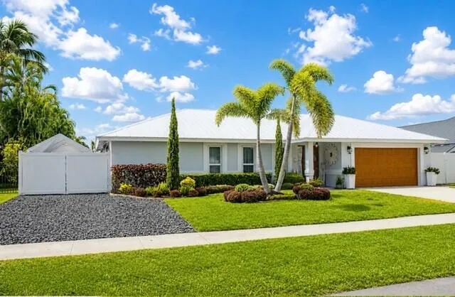Front exterior featuring a wood-finish garage door, well-maintained lawn, and mature palm trees