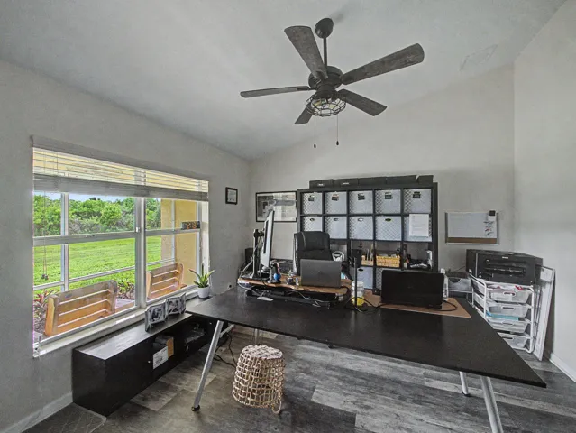 Vaulted ceiling with ceiling fan, large window with outdoor visibility, and laminate-finish flooring