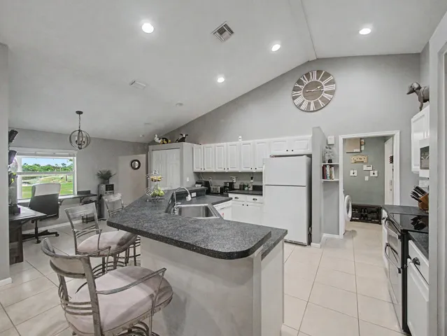 Vaulted ceiling, recessed lighting, white cabinetry, integrated kitchen island with sink, and tile flooring
