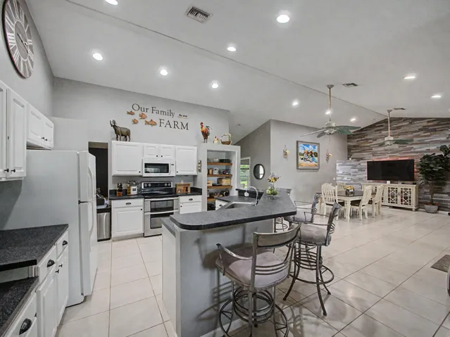 Vaulted ceilings with recessed lighting, white cabinetry, a built-in kitchen island with a dark countertop, a dining area with a stone-finish accent wall, and tiled flooring throughout