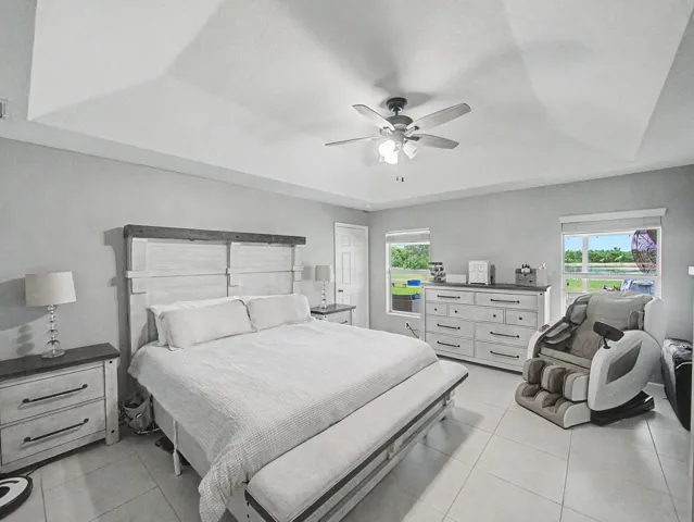 Tray ceiling, ceiling fan with lighting, tile flooring, two windows, and an interior door