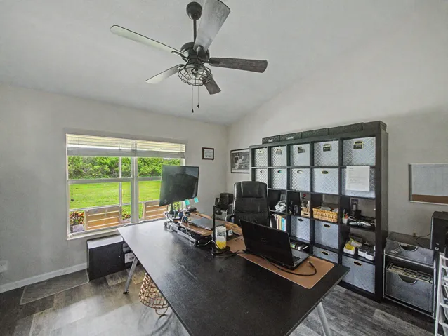 Vaulted ceiling with ceiling fan, large window with outdoor visibility, and laminate-finish flooring