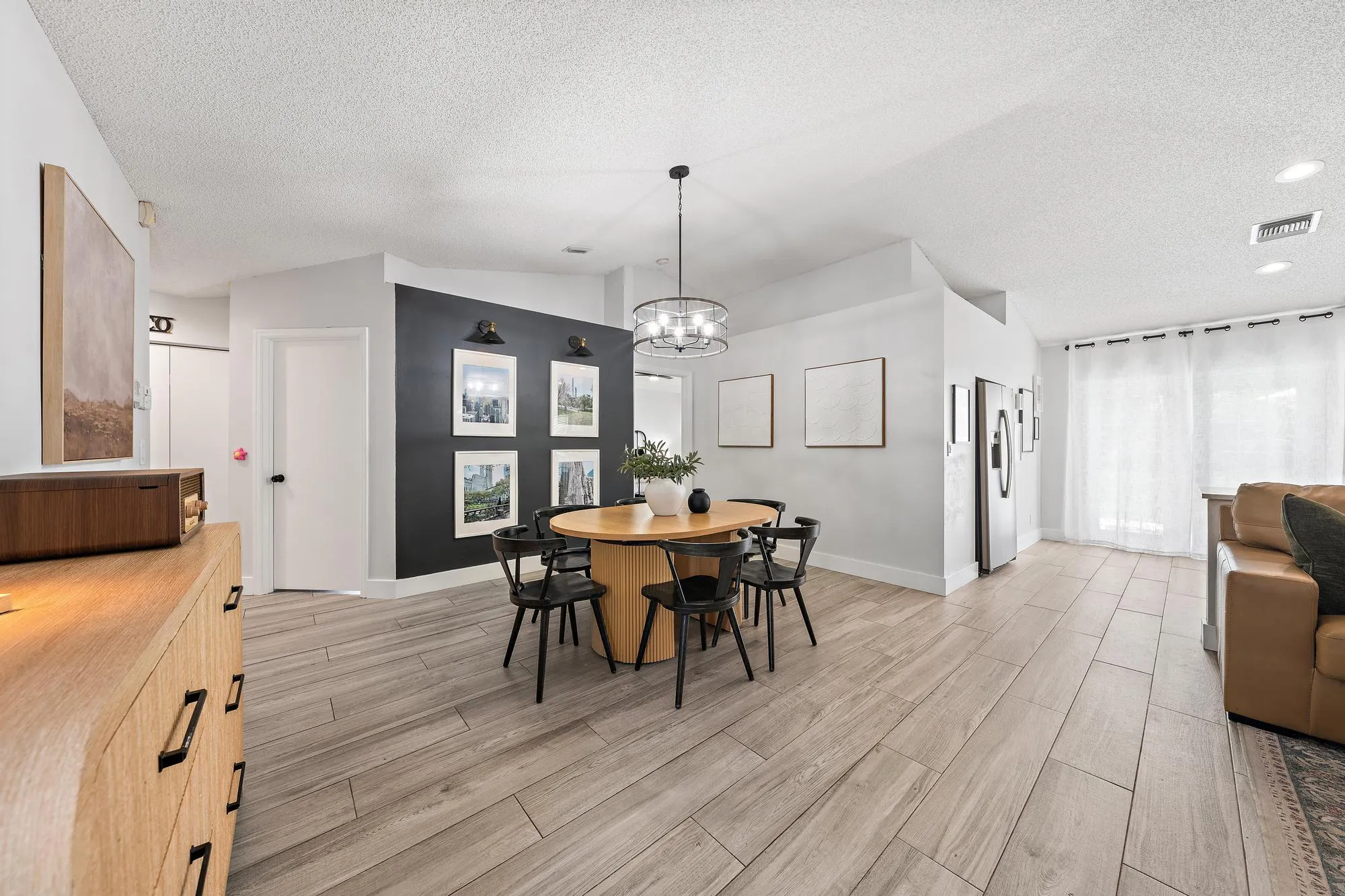 Open-concept living space with wood-finish flooring, a contemporary chandelier, recessed lighting, and a stainless steel refrigerator