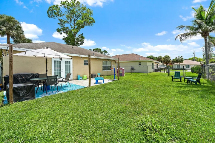 Expansive backyard featuring a concrete patio, double glass panel doors, and mature palm trees