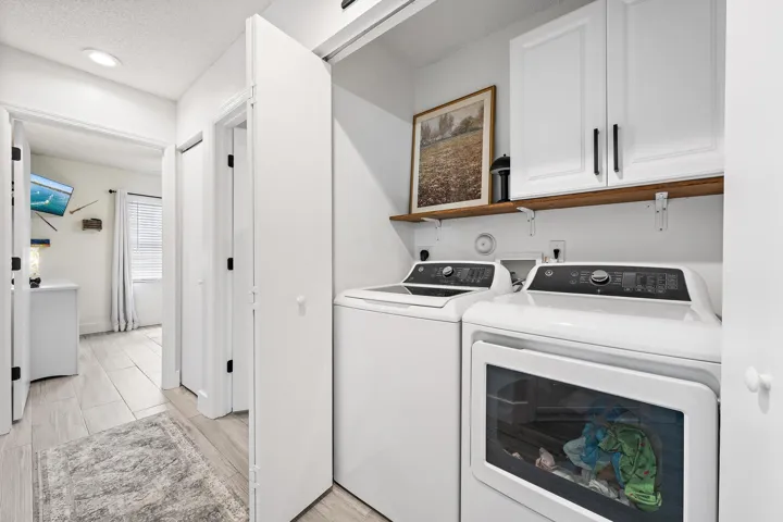 Dedicated laundry area featuring a washer and dryer, white cabinetry with dark hardware, and a wood-finish shelf