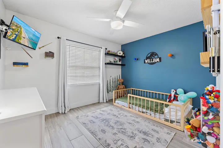 Room featuring wood-finish flooring, a ceiling fan, a window with blinds and curtains, and a painted accent wall