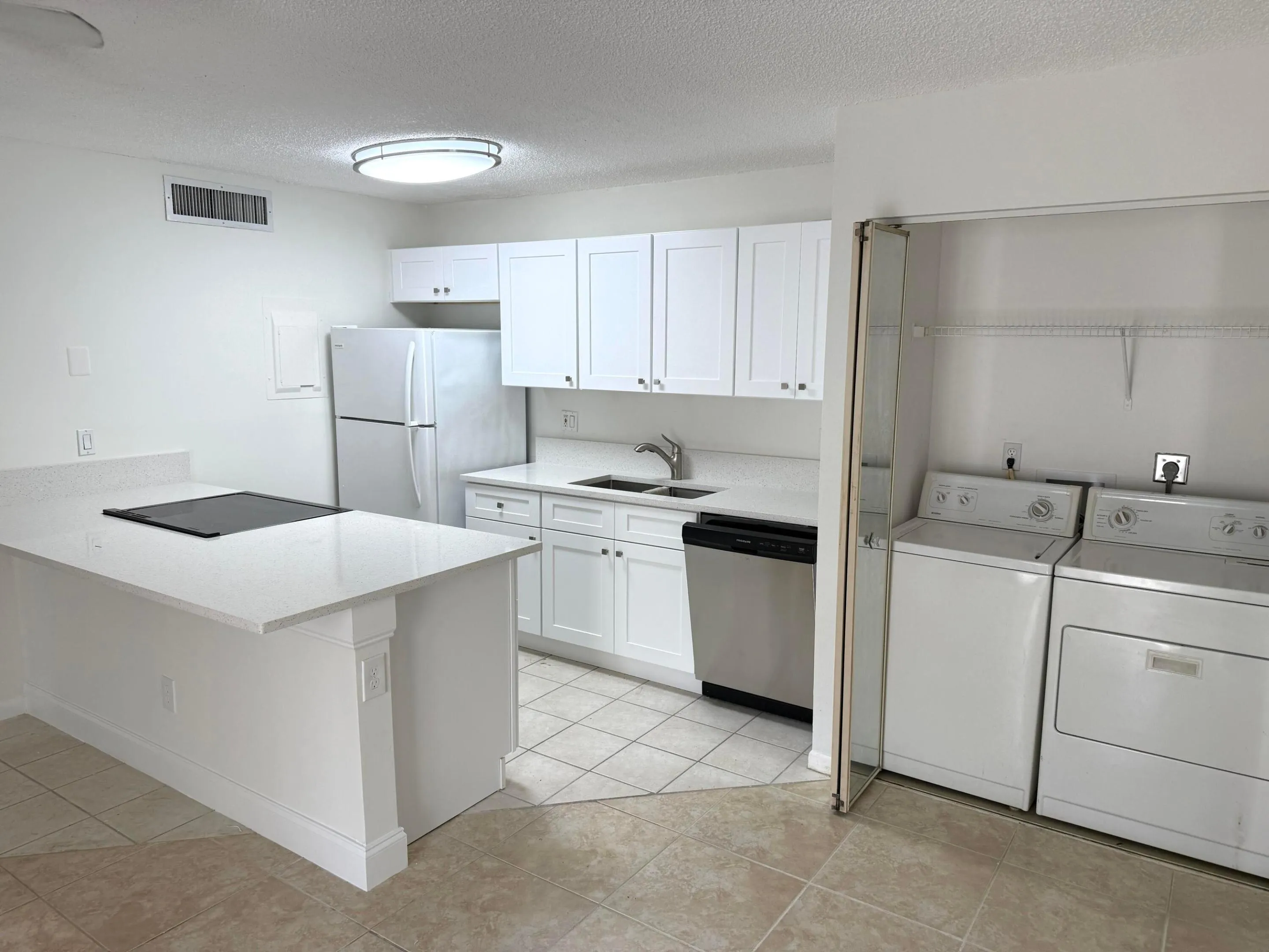 White kitchen cabinetry, light-toned countertops, tile flooring, built-in cooktop on island, and in-unit laundry appliances