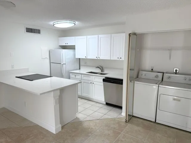White kitchen cabinetry, light-toned countertops, tile flooring, built-in cooktop on island, and in-unit laundry appliances