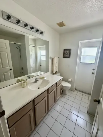 White tile flooring, single vanity with integrated sink, rectangular mirror, and a frosted glass exterior door
