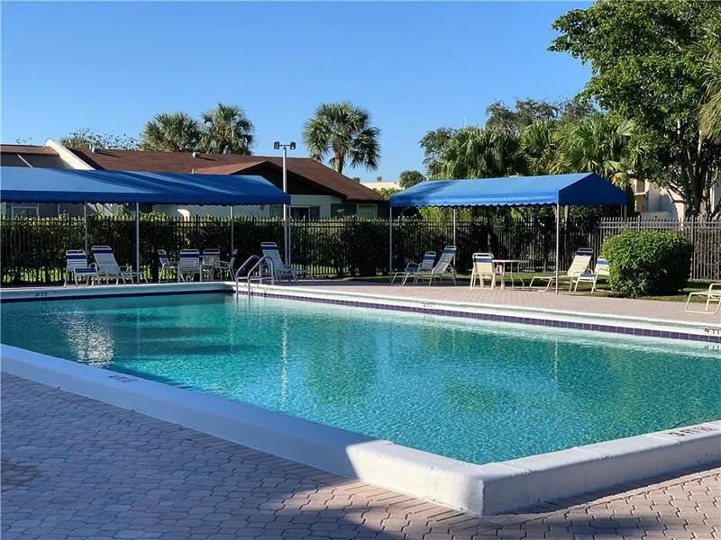 Resort-style swimming pool featuring a paver deck surround, integrated steps, and multiple shaded seating areas under blue canopies