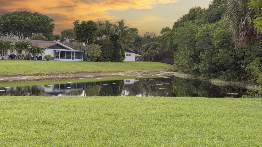 Expansive green lawn bordering a reflective body of water, with lush natural foliage and tropical trees providing a serene backdrop