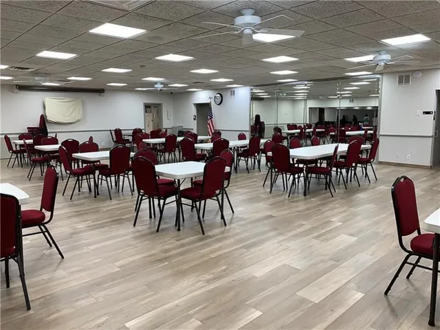 Spacious room featuring wood-finish flooring, drop ceiling with integrated lighting, and ceiling fans