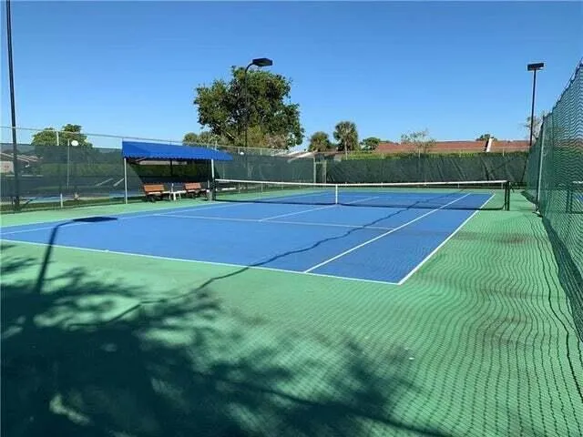 Two tennis courts featuring blue playing surfaces and green out-of-bounds areas
