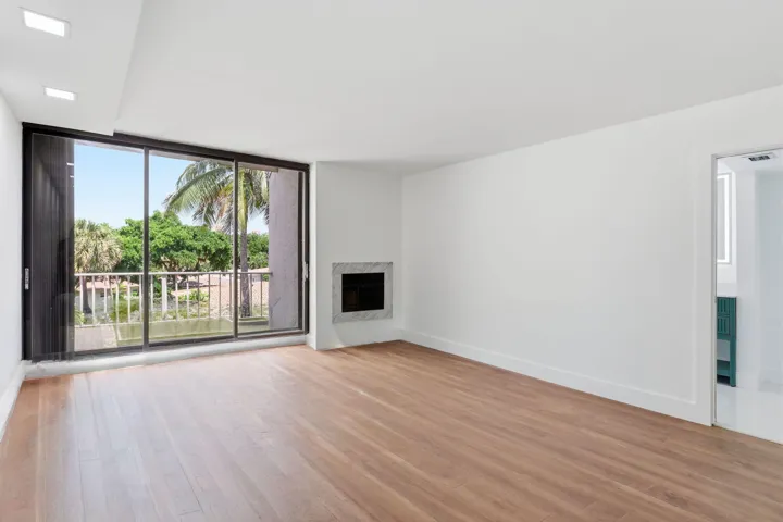 Wood-finish flooring throughout, recessed ceiling lighting, a built-in fireplace with a stone surround, and an expansive sliding glass door to the exterior balcony