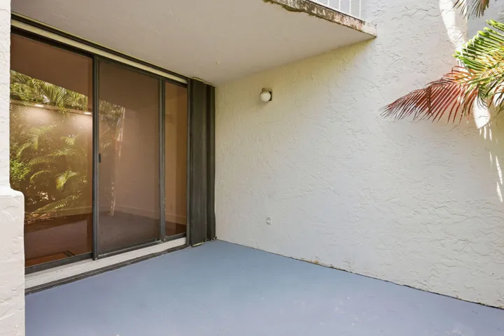 Sliding glass doors with screen, textured exterior wall, exterior wall light fixture, and concrete patio