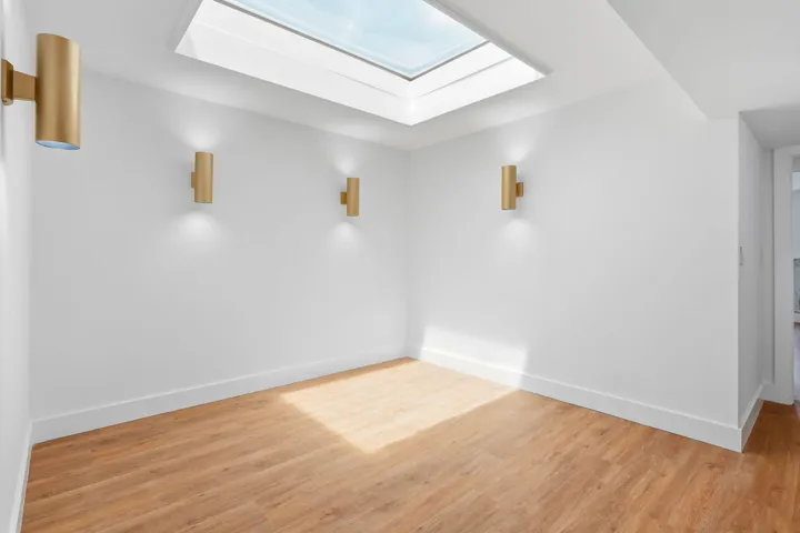 Skylight with natural light, wood-finish flooring, white walls, and three gold-tone wall sconces