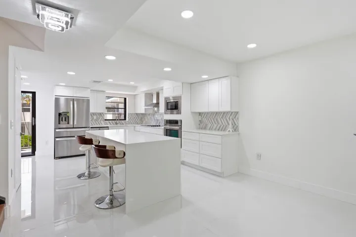 Contemporary kitchen featuring a large island, white cabinetry, stainless steel appliances, and a chevron tile backsplash