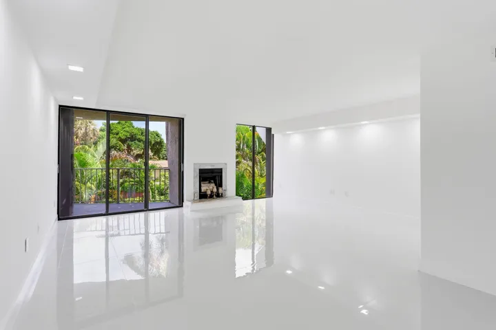 Expansive living area featuring reflective flooring, a decorative fireplace, and large sliding glass doors leading to an outdoor balcony with railings