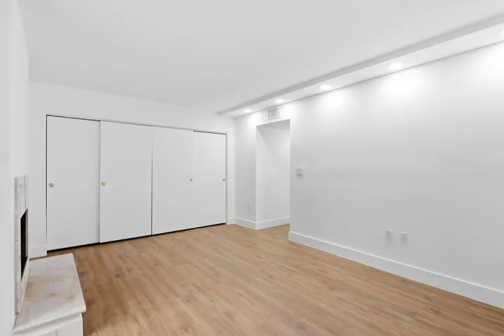 Recessed lighting, wood-finish flooring, white walls, built-in closet with sliding doors, and a fireplace with a stone surround