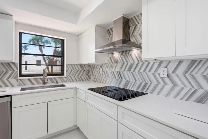 White shaker-style cabinetry with minimalist hardware, white countertops, and a full-height chevron-patterned tile backsplash